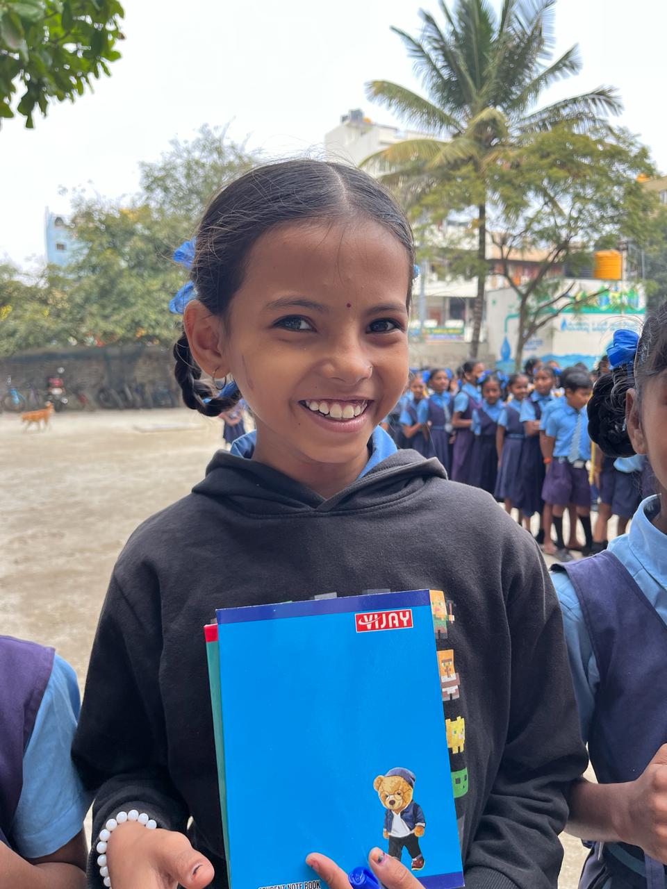 A smiling young girl holding her blue school notebook.